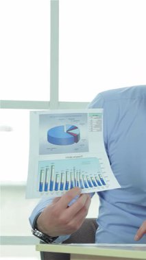 Parlak, modern bir ofiste, iki kendine güvenen iş adamı kapsamlı bir iş planını analiz ederek canlı bir tartışmaya girişirler. Bir adam, açık mavi gömlekli, tutkuyla renkli çizelgeler sergiliyor, diğeri ise parlak siyah bir takım elbise giyiyor.