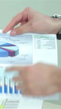 Yakın çekimde iki işadamı canlı grafikleri canlı bir iş raporunda tartışıyor, elleri coşkuyla hareket ediyor. Keskin resmi giysiler içinde ışıl ışıl, modern bir ofiste güven ve profesyonellik yayıyorlar.