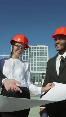 Parlak turuncu kasklar takmış üç kendine güvenen mimar, açık mavi gökyüzünün altındaki planları hevesle inceliyor. Canlı takım çalışmaları ve yenilikçi tartışmaları, şehir gelişiminin geleceği için heyecan yaratıyor.