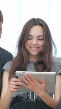 Genç profesyonellerden oluşan canlı bir üçlü, iki erkek ve bir kadın, zarif bir tabletle uğraşırken iş zaferlerini coşkuyla kutluyorlar. Işıl ışıl gülümsemeleri ve şık kıyafetleri modern bir ofis alanını aydınlatıyor.