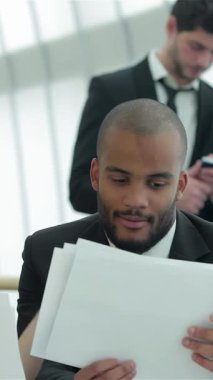 Gösterişli, çağdaş bir ofiste, kendine güvenen kızıl saçlı ve gözlüklü bir kadın, her ikisi de önemli belgeleri incelemeye dalmış, iyi giyimli bir adamla tutkuyla stratejilerini tartışıyor. Bu arada, iki profesyonel daha, odaklanmış bir adam ve...