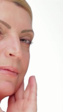 Zarif, orta yaşlı, beyaz bir kadın yanağını nazikçe okşuyor. Parlak tenini el değmemiş beyaz bir zemine vurguluyor. Bu büyüleyici portre güzellik ve kendine güven yayıyor, özgüvenin özünü ve zamansız zarafeti somutlaştırıyor.