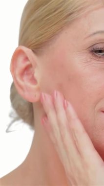 Zarif, orta yaşlı bir kadın nazikçe yanağını okşuyor, parlak cildini el değmemiş beyaz bir arka plana vurguluyor. Bu çarpıcı yakın plan portre güzelliği ve özgüveni yansıtıyor, özgüvenin özünü ve zamansız zarafeti somutlaştırıyor.