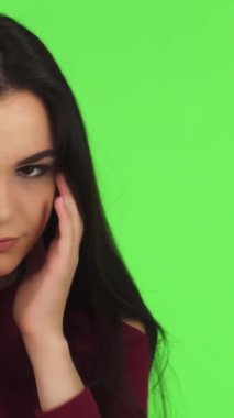 Çarpıcı, koyu renk saçlı genç bir kadın stüdyoda, şakaklarını canlı yeşil bir zemine sürterken gözle görülür bir şekilde şaşkına dönüyor. Yorgun ifadesi, modern hayatın zorluklarını somutlaştıran yorgunluk ve duygusal gerginlik yayıyor.