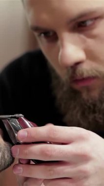 Şık bir berber dükkanında, kendini işine adamış bir berber müşterisinin sakalını ustalıkla yontuyor, titiz bir hassasiyet ve sanatçılık sergiliyor. Samimi ortam modern erkeksiliği ve kendine bakımı yansıtıyor. Odaklanmış berberle odaklı berber arasındaki ilişkiyi vurguluyor.