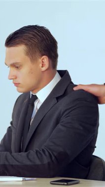 Gösterişli, çağdaş bir ofiste, genç bir erkek işadamı laptopuyla derinden meşgulken, destekleyici bir meslektaşı da takım çalışmasını sembolize ederek nazikçe omzuna elini koyuyor. Bu canlı sahne profesyonelliğin özünü özetliyor.