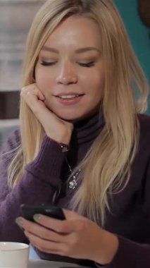 Büyüleyici bir kafede akıllı telefonuyla meşgul olan, dalgalı sarı saçlı, ışıl ışıl beyaz bir kadın. Sıcak, cezbedici atmosfer, onun hoş gülüşü ve buharı tüten bir fincan kahveyle mutlu bir anı yakalıyor.