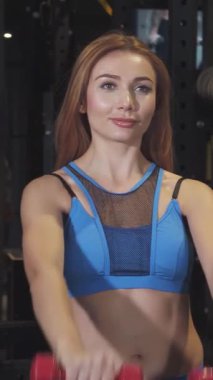 Gösterişli, modern bir spor salonunda, iki zinde genç kadın neşeli kırmızı dambıllar kaldırıyor, güçlerini ve dostluklarını sergiliyorlar. Işıl ışıl gülümsemeleri ve odaklanmış ifadeleri motivasyon ve güç yayar, dinamik bir fitness yolculuğunu somutlaştırır.