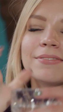 Çekici, beyaz, dalgalı sarı saçlı bir kadın ferahlatıcı, ışıl ışıl bir içecekten hoşlanıyor, düşünceli bakışları bir yana. Canlı renkler ve yumuşak, ılık aydınlatmalarla süslenmiş samimi kafe, davetkar bir ortam yaratıyor.