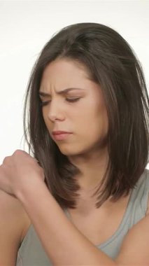 Kararlı genç bir kadın nazikçe omzunu uzatarak, spor yaparken sakatlık bilincinin kritik önemini vurguluyor. Kusursuz beyaz bir arka plana sahip olan atletik vücudu sağlıklı bir vücuda güç ve bağlılık yayıyor.