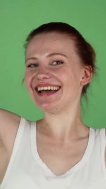 Canlı bir stüdyo çekiminde parlak kızıl saçlı genç bir kadın ışıl ışıl gülümsüyor ve coşkulu bir şekilde yeşil renkli bir arka plana karşı başparmak kaldırıyor. Bulaşıcı neşesi ve ruhsal enerjisi sahneyi aydınlatıyor.