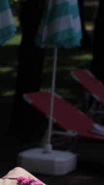 İki muhteşem beyaz kadın, biri esmer ve diğeri ateşli kızıl saçlı, ışıl ışıl bir havuzun yanındaki iskemlede güneşleniyorlar. Modaya uygun bikiniler ve şık plaj şapkaları giyip rahatlama ve neşe saçarak sıcacık havayı emiyorlar.