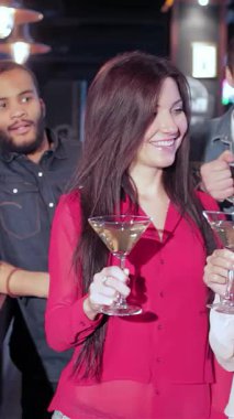 Genç erkek ve kadınların hareketli bir barda toplanması, neşeli bir şekilde kadehlerini kaldırmaları. Renkli dekorlar ve neşeli tezahüratlarla çevrili favori futbol takımlarına tezahürat ederken hava heyecanla dolup taşıyor.