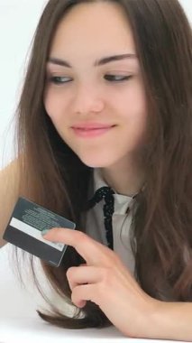 Uzun, dalgalı saçları olan şık bir genç kadın, kredi kartını parlak dizüstü bilgisayarına yakın tutarak güvenli bir şekilde online alışveriş yaparken mutluluk saçıyor. Parlak, minimalist arkaplan heyecanını artırıyor, modern çağın özünü yakalıyor.