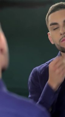 Taze saç kesimi olan tatlı bir genç adam parlak bir berber aynasında yansımasına hayranlık duyuyor. Cazibesi ve kendine güveni tam. Canlı ve modern ortam, tımar etmenin sanatını ön plana çıkarıyor. Kendine bakmanın modaya uygun bir şey olmasını sağlıyor.