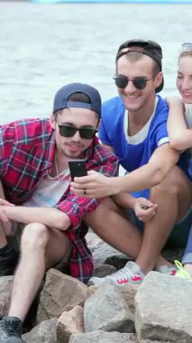 Üç canlı arkadaş, iki erkek ve bir kadın, güneşin öptüğü kayalık kıyılarda bir selfie çekerken mutluluk saçıyorlar. Bulaşıcı kahkahaları rüzgarda dans eder, suyun ışıl ışıl arka planına karşı sevgi dolu anılar yaratır.