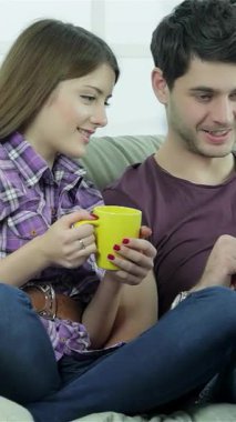 Genç ve hayat dolu bir çift, parlak sarı bir fincan çayla, parlak bir laptopta e-postaları okurken gülücüklerini ve kahkahalarını paylaşıyor. Rahatlamış tavırları ve hareketli ifadeleri sıcak, davetkar bir atmosfer yaratıyor.