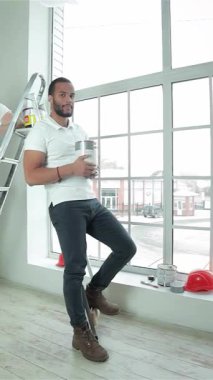 İki hevesli genç müteahhit, biri merdiven üzerine tünemiş, diğeri de büyük bir pencerenin yanında, hem boya kutuları hem de parlayan başparmaklar tutan ferah, güneşli bir dairede güven içinde duruyorlar. Parlak gülümsemeleri ve enerjik enerjileri ruhu somutlaştırıyor.