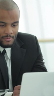 Keskin siyah takım elbiseli kararlı bir işadamı, bilgisayarındaki verileri dikkatle inceleyerek çağdaş ve parlak bir ofiste çalışıyor. Temiz çizgiler ve doğal ışık ilham verici bir atmosfer yaratarak, onun başarıya ve yeniliğe olan bağlılığını vurguluyor.