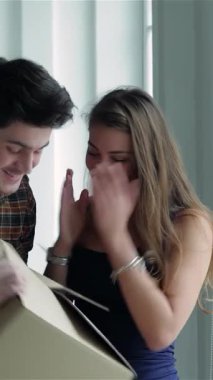 Genç bir çift, güneşli bir pencerenin yanında duruyor, bir kutu tutuyorlar ve yeni dairelerinde paketlenmemiş karton kutularla çevrili, parlak gülümsemelerle dışarı bakıyorlar. İfadeleri saf neşe ve heyecan yayar, gemiye binmenin özünü yakalar.