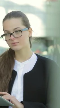 Gösterişli resmi giysiler içinde dengeli ve kendinden emin bir iş kadını, dışarıda duruyor, tabletini dikkatle gözden geçirirken yeni ortaklarını karşılamaya hazırlanıyor. Düşünceli ifadesi ve mesleki tavırları heyecan saçıyor.