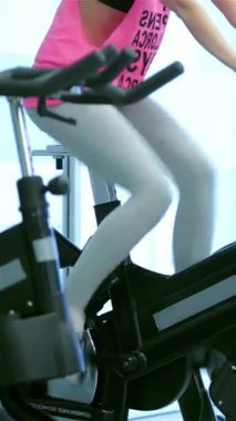 Dinamik fitness sınıfında hareketsiz bisiklete binen, güç ve birlik saçan atletik kadınlar var. Renkli spor kıyafetleri ve kararlı ifadeleri heyecan verici bir atmosfer yaratıyor ve sağlığa olan bağlılıklarını gösteriyor.