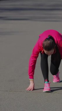 Kararlı genç bir kız heyecan verici bir koşuya başlamak üzere bir stadyum pistinin canlı başlangıç çizgisinde çömeliyor. Pembe elbisesi pürüzsüz gri yüzeye çarpıyor. Rekabetin heyecanını ve özünü somutlaştırıyor.