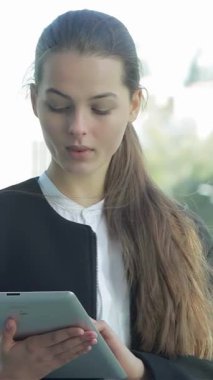 Kendine güvenen bir iş kadını açık havada duruyor, tabletinde partnerleriyle derin bir ilişki içinde, profesyonellik ve kararlılık yayıyor. Arkasındaki canlı şehir manzarası başarı ve işbirliği atmosferini güçlendiriyor ve onun önemli önemini vurguluyor.