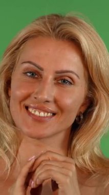 Çekici, olgun, dalgalı sarı saçlı bir kadın kameraya şşşş yapar. Neşeli gülüşü sıcaklık ve cazibe saçar. Canlı yeşil bir krom anahtara karşı duran zarif jesti entrika ve flörtleşmeye davetiye çıkararak büyüleyici bir...