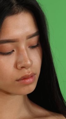 Işıl ışıl, uzun, parlak siyah saçlı genç bir Asyalı kadın kameraya sıcak bir şekilde gülümsüyor. Kusursuz cildi parlak yeşil renkli bir arka planda parlıyor. Neşeli ifadesi ve büyüleyici güzelliği pozitifliği ve gençlik enerjisi, davetkar