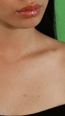 Çarpıcı bir yakın plan, güzel, genç Asyalı kadın, uzun, parlak saçlı, düşünceli, yeşil renkli bir arka plana doğru bakıyor. Sakin ifadesi, parlak dudakları ve narin köprücük kemiği özgüven ve cazibe yayıyor.