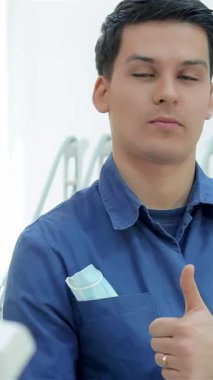 Kendine güvenen bir dişçi, modern, iyi ışıklandırılmış bir klinikte ışıldayan diş aletleriyle çevrelenmiş, sıcak bir gülümsemeyle baş parmak kaldırıyor. Bu davet sahnesi pozitifliği ve profesyonelliği yansıtıyor, dişçilerin olağanüstü adanmışlığını vurguluyor.