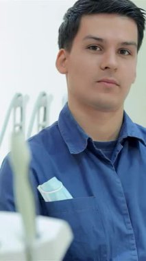 Gıcır gıcır mavi üniformalı kendine güvenen bir erkek dişçi parlak bir gülümsemeyle modern bir diş muayenehanesinde onay veriyor. Işıldayan diş aletleri ve el değmemiş çevre, hastaları rahatlamaya ve hissetmeye davet eden hoş bir atmosfer yaratıyor.