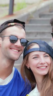 Genç arkadaşlardan oluşan canlı bir üçlü, güneşli açık hava basamaklarında, şık şapkalarını ve güneş gözlüklerini sergileyerek selfie çekerken neşe saçıyor. Bulaşıcı gülümsemeleri ve şakacı arkadaşlıkları kaygısız bir yaz gününün özünü özetliyor.