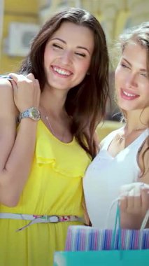 İki şık kız, renkli alışveriş torbalarıyla güneşli caddede parlarken neşe saçıyor. Bulaşıcı kahkahaları ve kaygısız ruhları arkadaşlığın heyecanını ve hoş bir alışveriş macerasını simgeliyor.