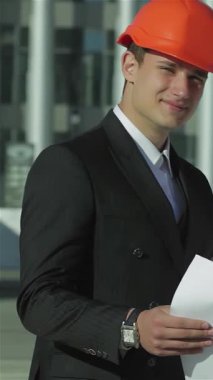 Üç kendine güvenen mimar, parlak turuncu miğferler takmış, şevkle planlarını gözden geçiriyorlar, takım çalışması ve profesyonelliği somutlaştırıyorlar. Bu yenilikçi yapının geleceğini öngördüklerinde dinamik işbirlikleri enerji yayıyor.