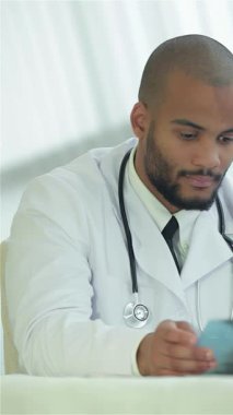 El değmemiş beyaz önlüklü ciddi bir doktor göğüs röntgenini dikkatle inceliyor, parlak ve modern bir klinikte bir hastayla anlamlı bir diyalog kuruyor. Atmosfer profesyonellik ve özen gösteriyor ve sağlığın kritik önemini vurguluyor.