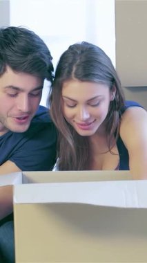 Neşeli bir çift yeni evlerinin zemininde oturmuş, zevkli hazinelerle dolu bir karton kutuyu hevesle keşfediyorlar. Etrafı boş duvarlarla ve istiflenmiş kutularla çevrili. Parlak gülümsemeleri yeni başlangıçların heyecanını ve sıcaklığını yakalıyor.