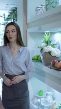 Yetenekli bir kadın çiçekçi, şık bir çiçekçide müşterisine çarpıcı çiçek aranjmanları, taze meyveler ve zarif mumlar sunar. Sahnede biri uzun, dalgalı saçlı, şık bir bluz giyen iki kadın yer alıyor.