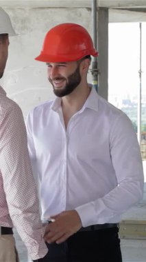 Gıcır gıcır beyaz gömlekli genç bir mimar ve parlak turuncu şapkalı bir müteahhit, inşaat alanının canlı kaosu arasında sıkı bir tokalaşmayı paylaşıyor. Bu dinamik işbirliği anı yapı iskelesi ve inşaat malzemeleriyle çerçevelenmiştir.