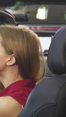 Genç, ışıl ışıl bir kadın saçlarını aynada ayarlarken, üstü açık şık arabasında otururken zevkle ışıldıyor. Bu canlı sahne yeni mülkiyetin heyecanını özetliyor, heyecan verici özgürlüğünü kucaklarken onun heyecanını vurguluyor