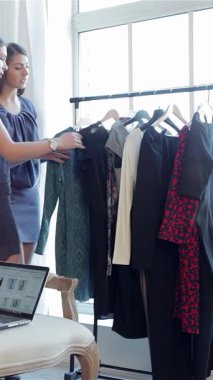 Kendine güvenen bir kadın şık bir kanepede dizüstü bilgisayarla uzanırken şık arkadaşları da heyecan verici bir şekilde yakındaki elbiseleri karıştırıyor. Bu canlı sahne arkadaşlığın neşesini ve online alışverişin heyecanını yayıyor, modern ortama uyum sağlıyor.