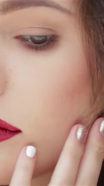 Güzel, beyaz bir kadının büyüleyici yakın çekimi kusursuz tenini nazikçe okşuyor özgüven ve zarafeti somutlaştırıyor. Çarpıcı kırmızı dudakları ve parıldayan gümüş tırnakları derin siyah arka planda büyüleyici bir kontrast oluşturuyor.