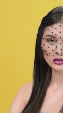 Göz kamaştırıcı peçeli bir kadın zarif bir şekilde başını kameradan çevirir ve büyüleyici özelliklerini canlı sarı bir arka plana karşı gözler önüne serer. Bu çekici esmer model, çıplak omuzlu ve çarpıcı makyajlı, gizem ve entelektüellik yayıyor.