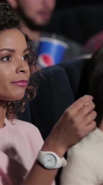 Canlı iki kız arkadaş, film gecesi maceralarına dalmış bulaşıcı kahkahalar ve patlamış mısır paylaşıyor. Samimi tiyatro heyecanla uğulduyor, ekranlar tarafından aydınlatılıyor, neşeli ifadelerini ve renkli patlamış mısırlarını vurguluyor.