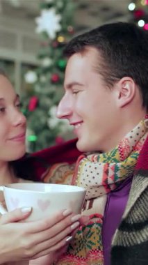 Hoş, genç bir çift sıcak bir battaniyenin altına kıvrılıp birbirlerinin gözlerinin içine bakarken güzel süslenmiş bir Noel odasında dumanı tüten kupaları sallıyorlar. Parıldayan peri ışıkları ve canlı bir ağaç aşkı kutlayan sihirli bir ortam yaratır.