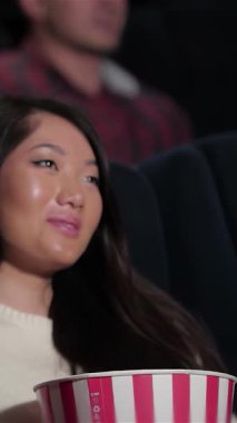 Asyalı bir kadın, gülücüklerle dolu sıcak bir sinemada neşeyle parlayan kız arkadaşına tatlı sözler fısıldamak için yaklaşır. Canlı bir izleyiciyle çevrelenmiş, patlamış mısır ve sodanın tadını çıkarıyorlar, tamamen sinematik sihre dalmışlar.