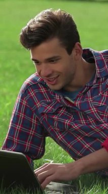 Neşeli genç bir adam, altın güneş ışığı sahneyi yıkarken dizüstü bilgisayarıyla dolu canlı yeşil çimenlerde rahatlıyor. Bu pitoresk park manzarası boş zamanların ve verimliliğin mükemmel bir karışımını yakalıyor, açık havada çalışmanın keyfini gösteriyor.