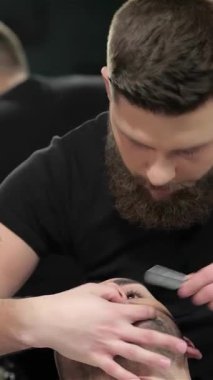 Eski moda bir dekorla süslenmiş şık bir berber dükkanında, yetenekli bir berber, genç bir adamın sakalını ustalıkla tıraş eder, gelenekle modern tarzı harmanlar. Sahne, berberlerin karmaşık dövmeleriyle vurgulanmış sıcak bir ambiyansla dolu.