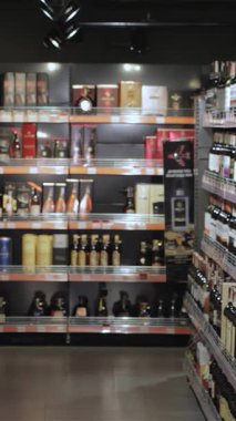 Genç bir çift hipermarketin hareketli alkol reyonunda geziniyor, tramvayları taze ürünlerle dolup taşıyor. Sakallı adam bir şişeyi entrikayla incelerken kız arkadaşı da ona doğru eğilip paylaşılan keyifli bir an yaratıyor.